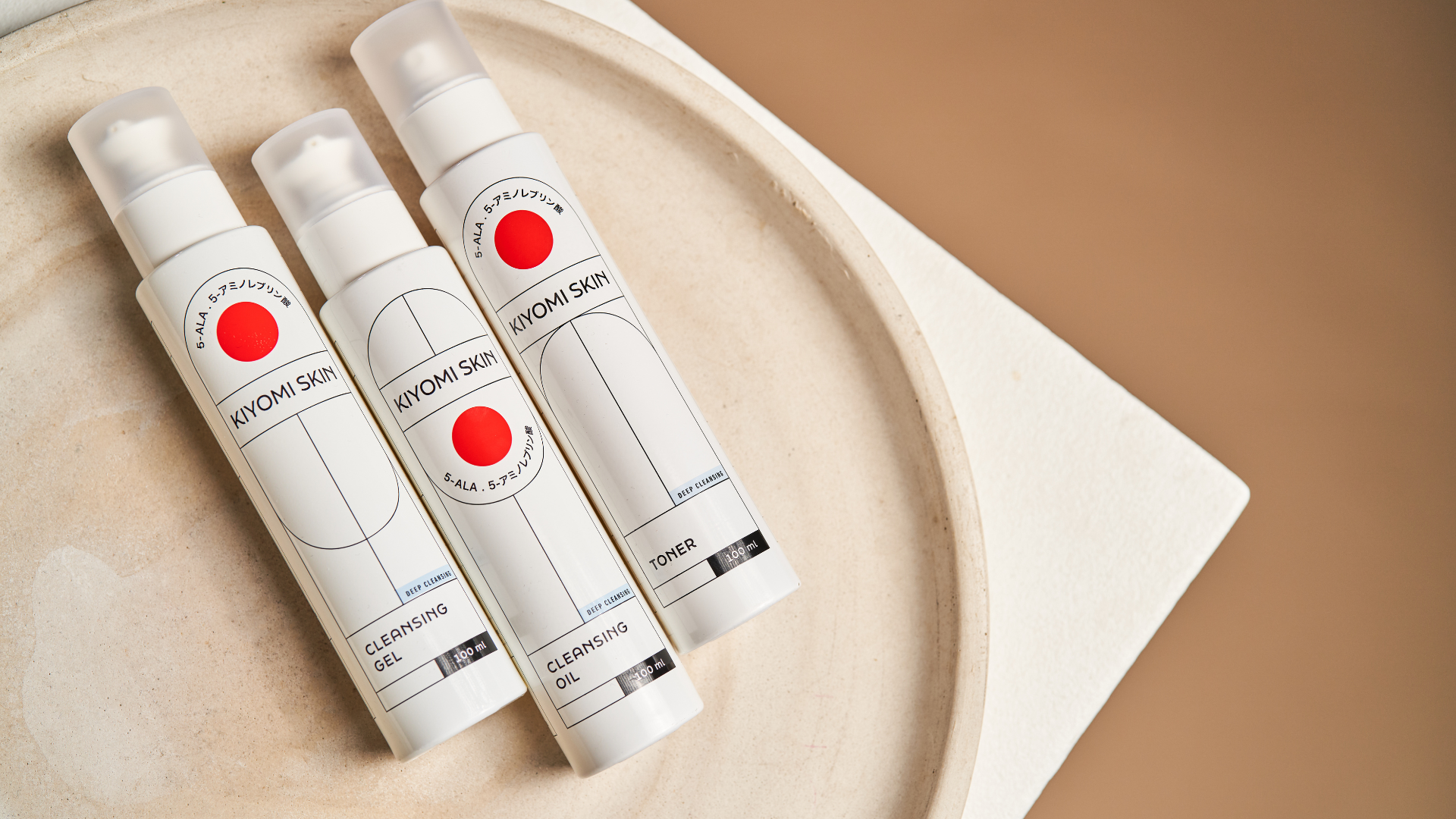 Three bottles of KIYOMI SKIN skincare products arranged on a round beige tray.