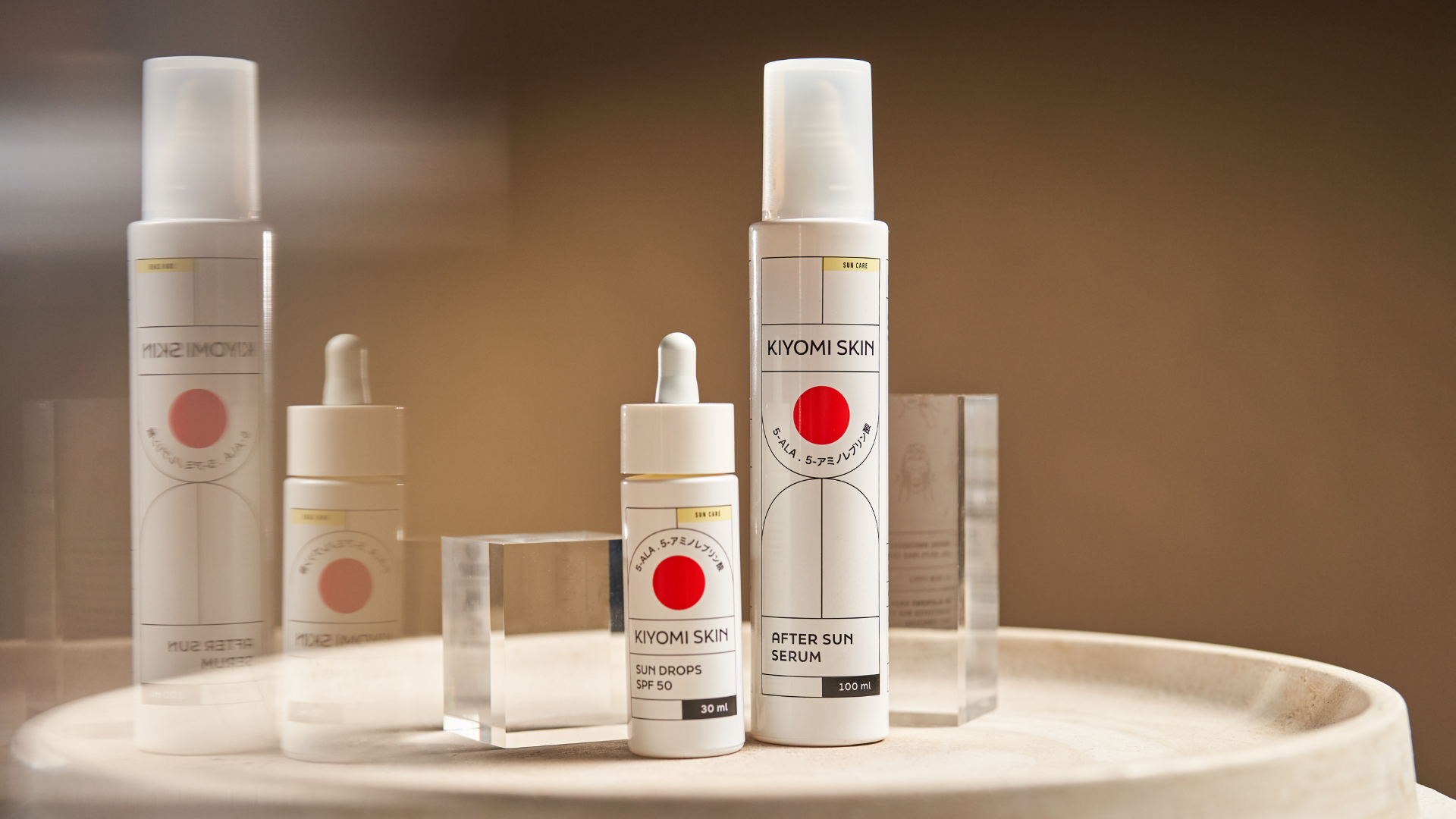 Two Kiyomi Skin skincare bottles with white labels and red circles, placed on a round wooden surface.