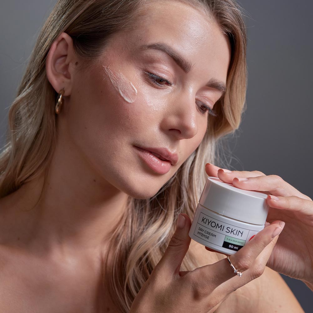 Woman applying Kiyomi Skin day cream to her cheek, holding the cream jar in her hand.