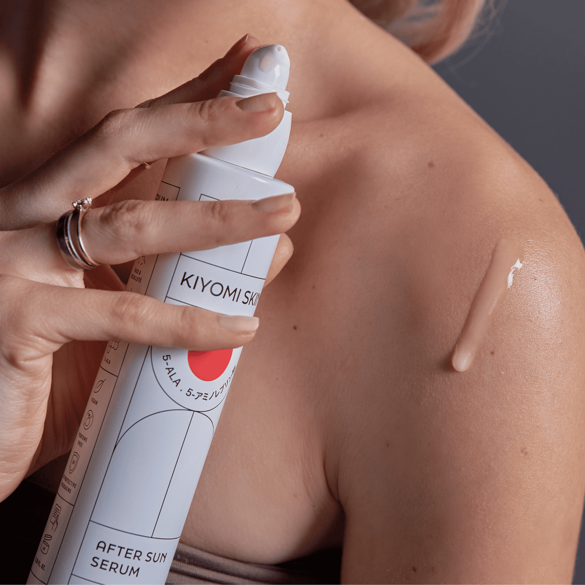Eine Person trägt das After-Sun-Serum aus einer SBI-ALApromo-Flasche auf ihre nackte Schulter auf und versorgt ihre Haut so mit Feuchtigkeit und den beruhigenden Wirkungen von 5-ALA.