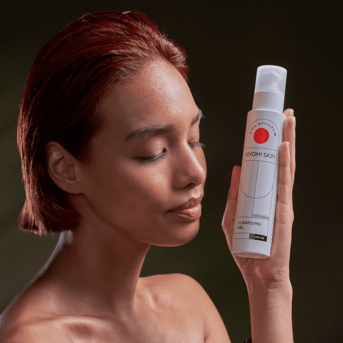 Eine Frau mit geschlossenen Augen hält eine Flasche „SBI ALApromo Cleansing Gel“ vor ihrem Gesicht vor einem dunklen Hintergrund und verkörpert damit die Essenz einer sanften Gesichtsreinigung.