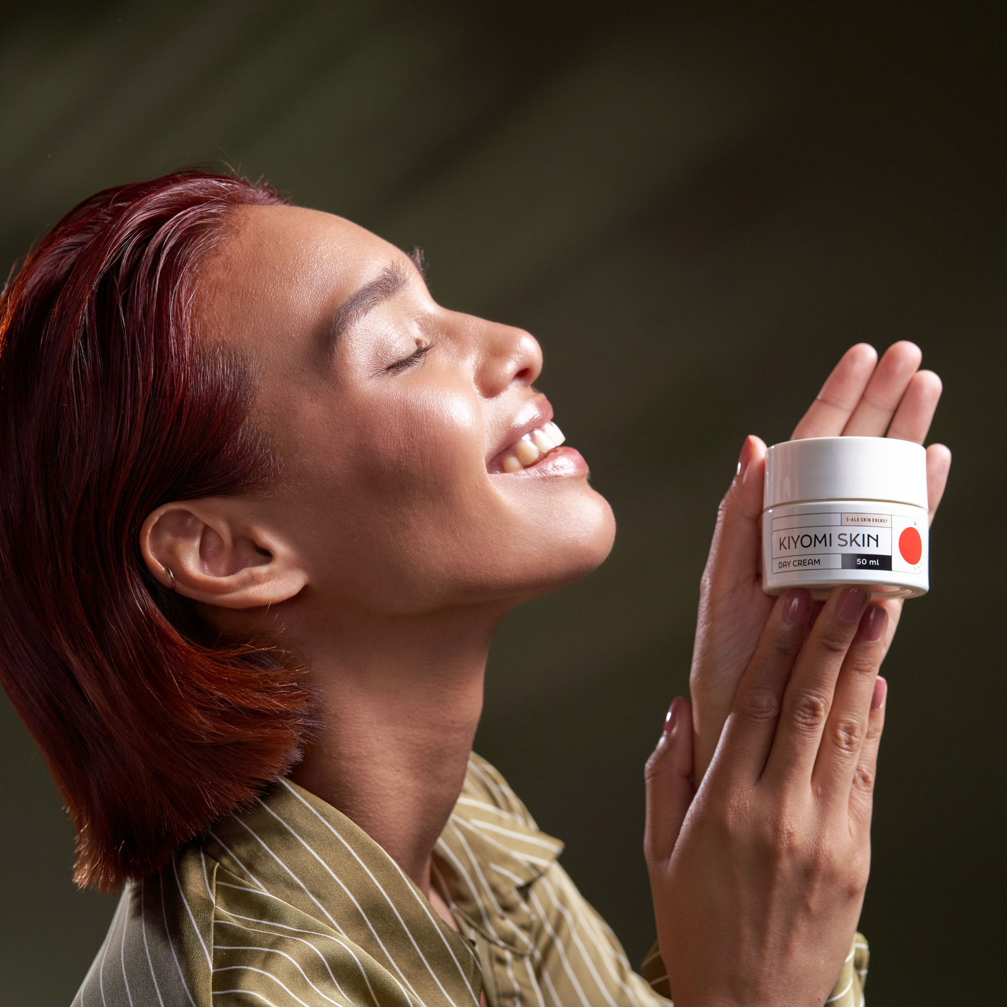 A smiling person with glowing skin holds a Day Cream jar against a soft green background.