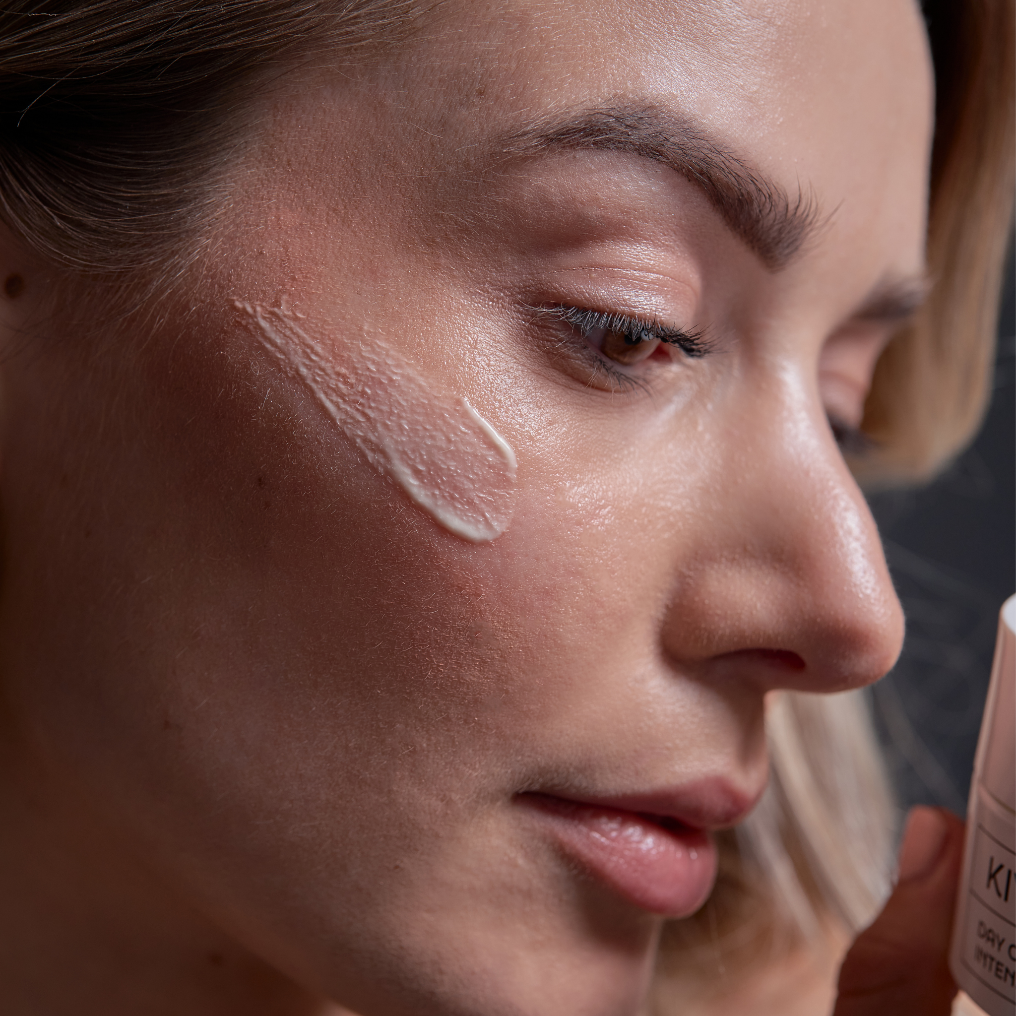 Close-up of a woman applying Day Cream Intense to her cheek, highlighting smooth skin and natural makeup—perfect for intensive facial care, especially for sensitive skin.