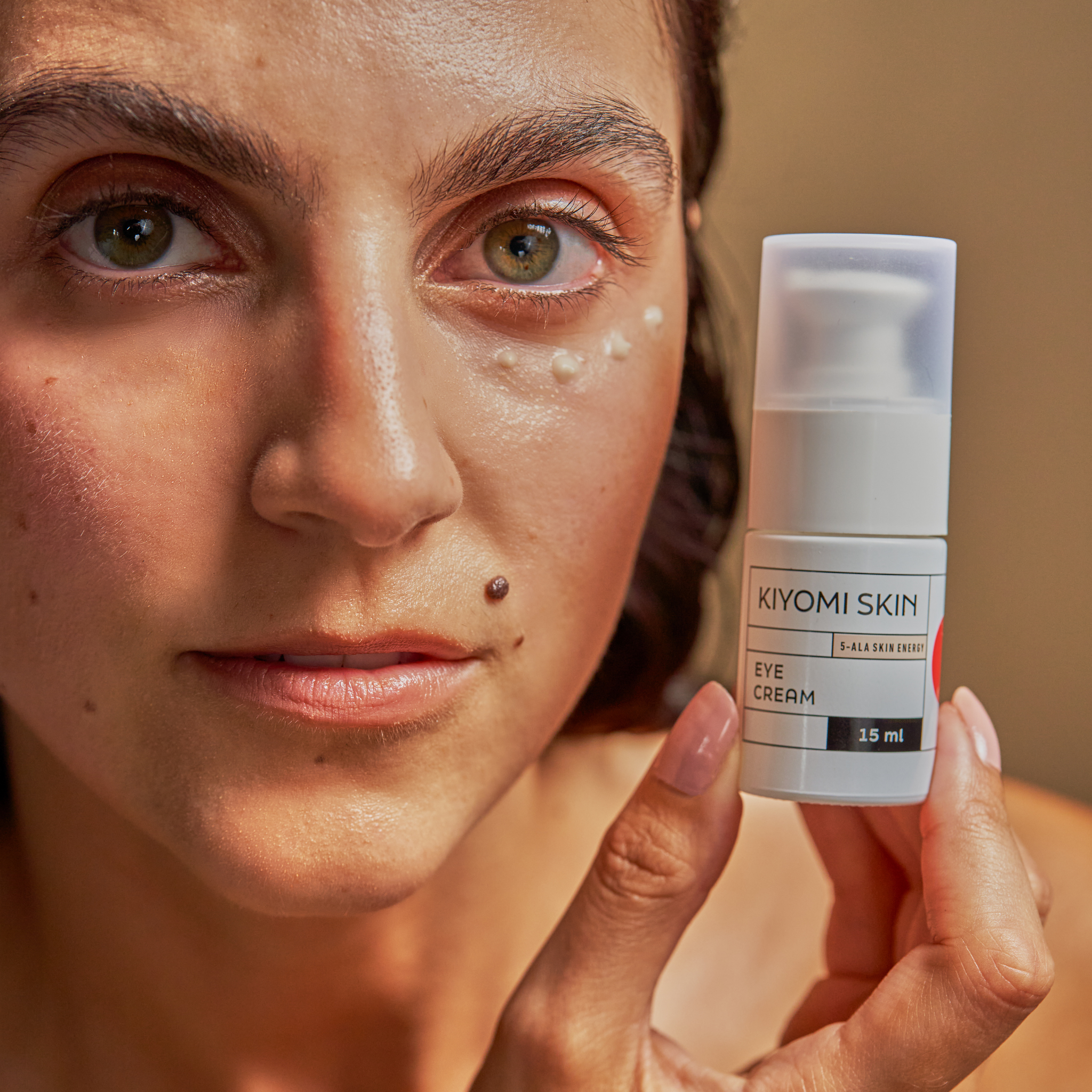 Woman applies dots of eye cream while holding the Hydra Energy Trio bottle near her face—an essential step in her fragrance-free moisturizing routine.