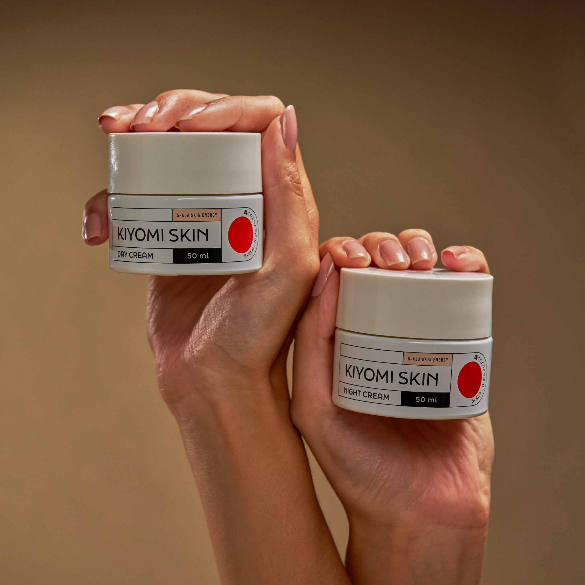 Two hands hold Midnight Magic & Morning Bright jars against a plain beige background, highlighting essential moisture care for skin regeneration.