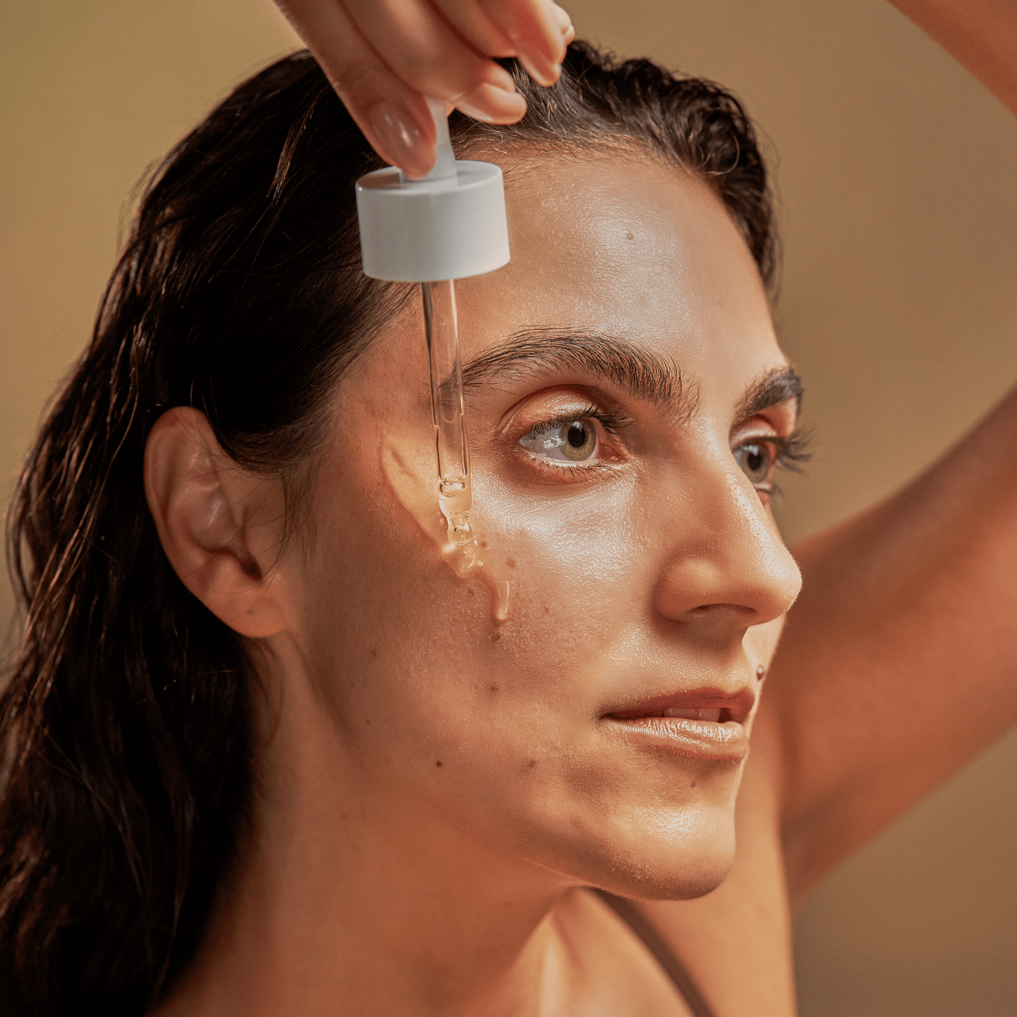 A woman applies Moisturizing Serum to her cheek using a dropper.