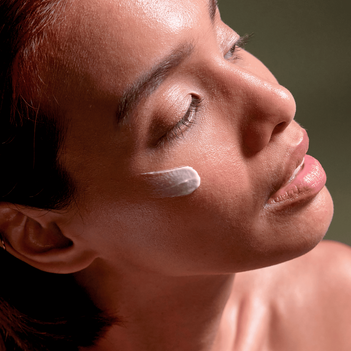 Eine Frau mit geschlossenen Augen hat einen Tupfer der SBI ALApromo Nachtcreme auf der Wange, was ihre glatte, strahlende Haut unterstreicht – ideal für empfindliche Haut und mit feuchtigkeitsspendender Wirkung.