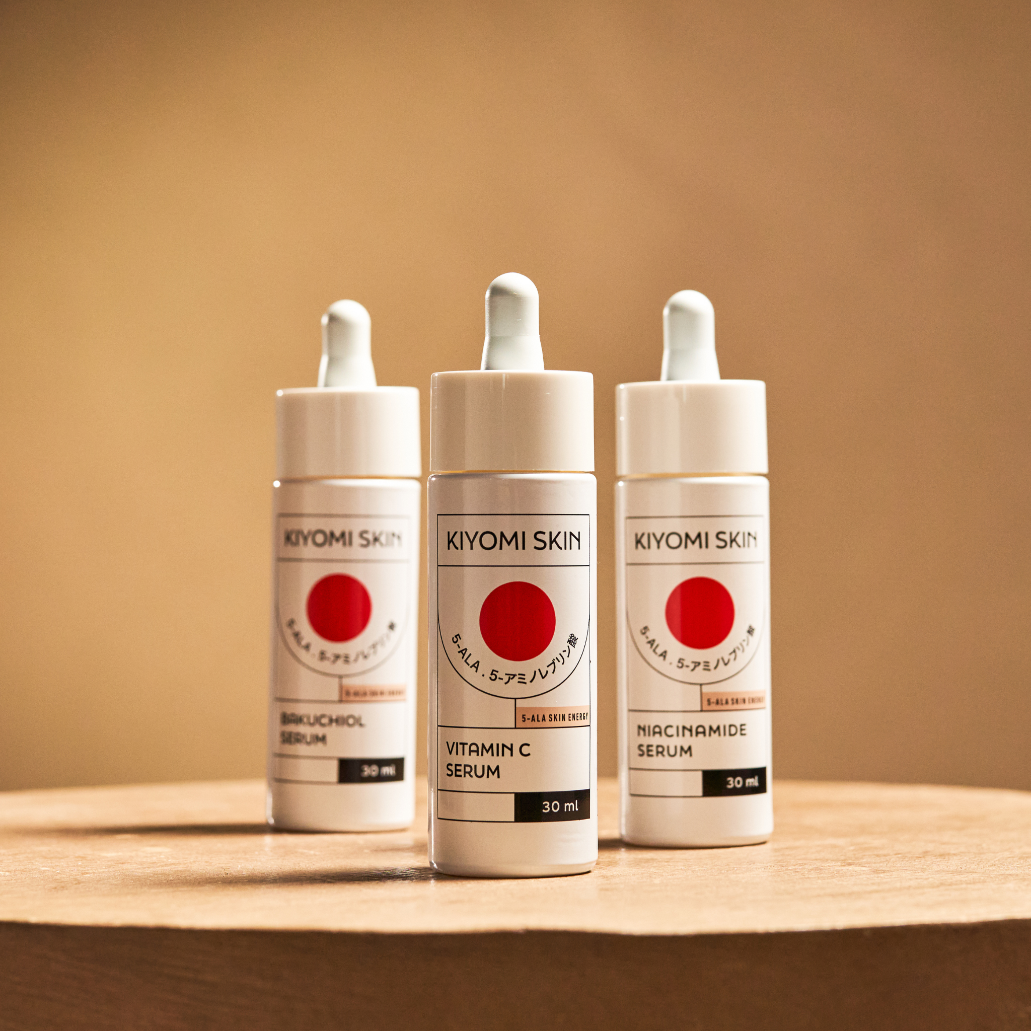 Three Serum Trilogy Radiance & Renewal bottles with droppers sit on a wooden surface against a beige background, showcasing the nourishing power of Bakuchiol and Vitamin C.