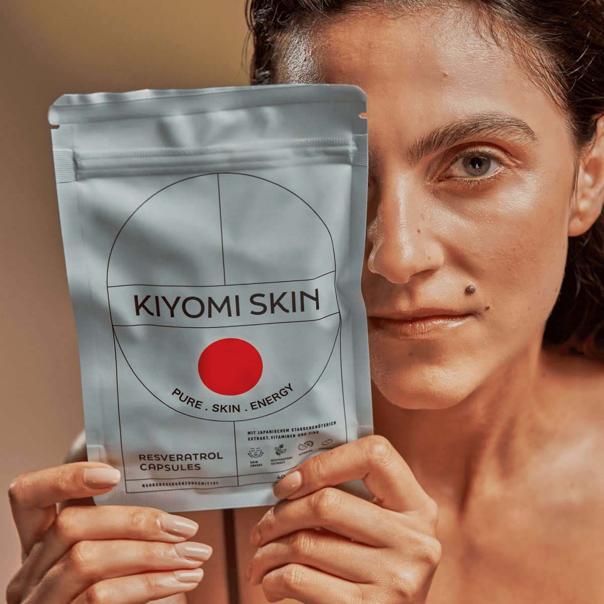 Eine Frau, die eine Tüte mit SBI ALApromo Skin Energy Resveratrol-Kapseln (MHD 09/2026) nahe an ihr Gesicht hält und in die Kamera blickt – ein Bild, das die Kraft des antioxidativen Zellschutzes für gesunde Haut perfekt einfängt.