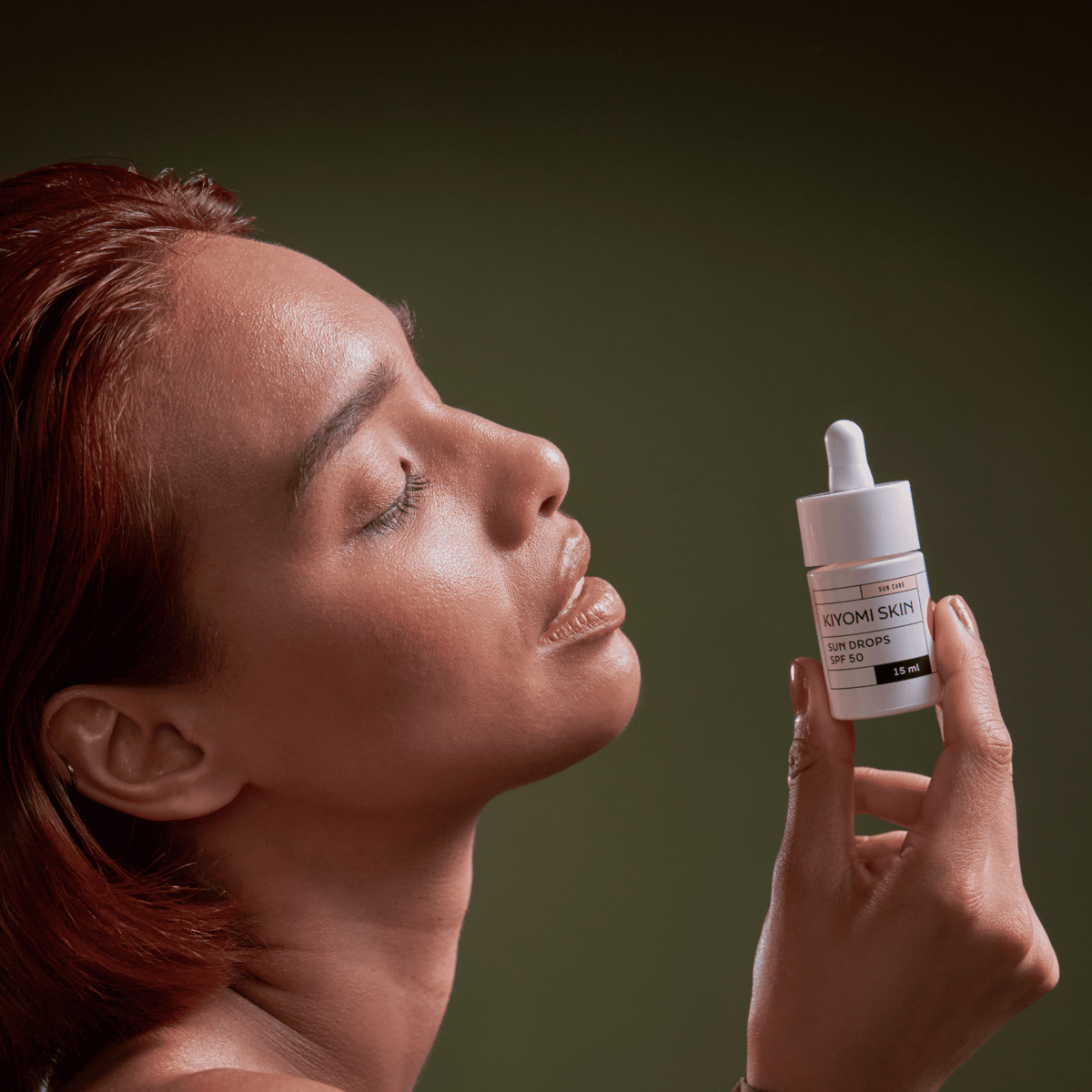 Eine Frau mit geschlossenen Augen hält eine SBI ALApromo Travel Size Sun Drops SPF 50-Serum-Tropfflasche nahe an ihr Gesicht und hebt damit die leichte Textur und den zuverlässigen UV-Schutz dieses leichten Sonnenschutzmittels hervor.