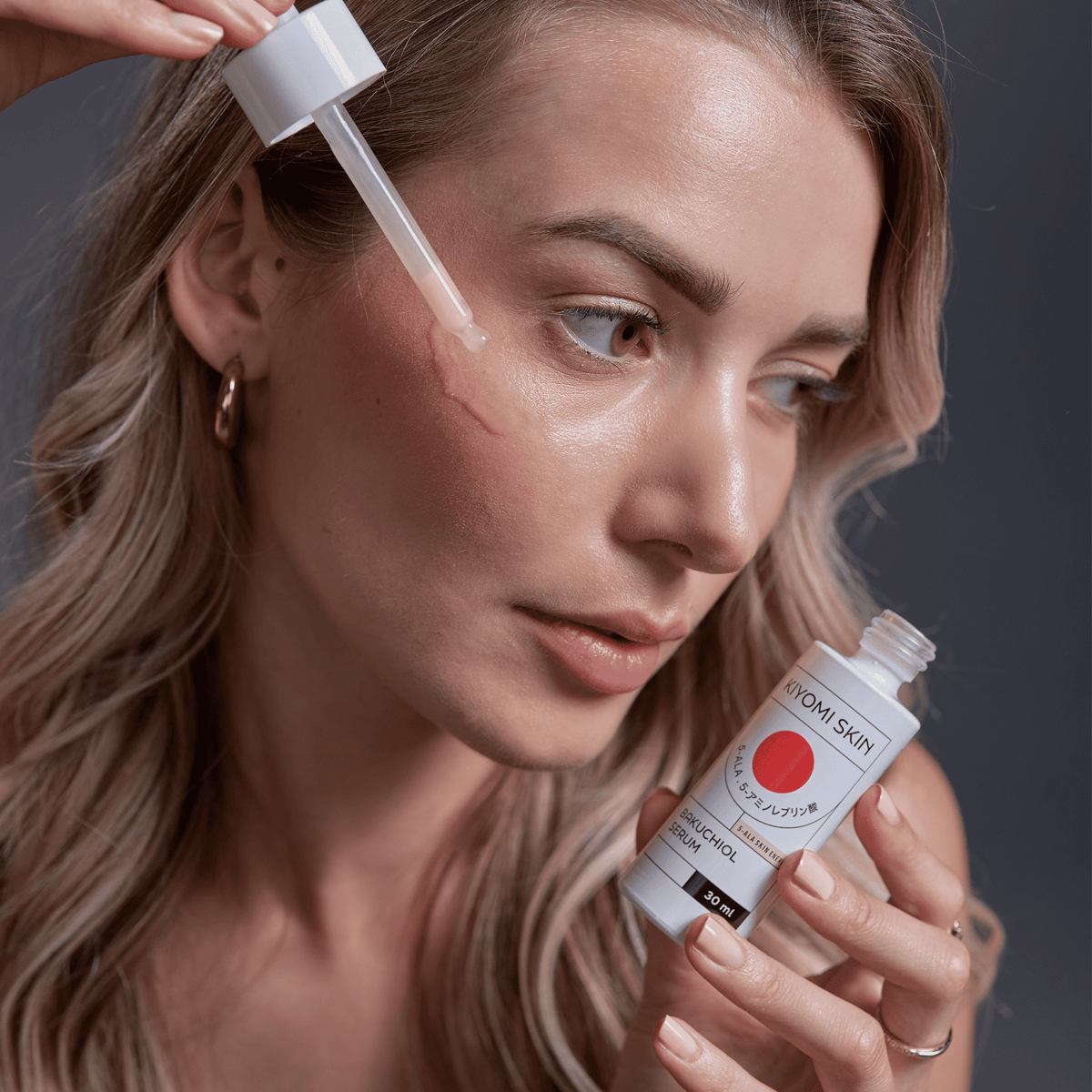 Eine Frau trägt das SBI ALApromo Bakuchiol-Serum – eine sanfte Retinol-Alternative – mit einer Pipette auf ihre Wange auf, während sie die Hautpflegeflasche in der anderen Hand hält. Dieses speziell für empfindliche Haut entwickelte Serum bietet wirksame Pflege ohne Hautirritationen.