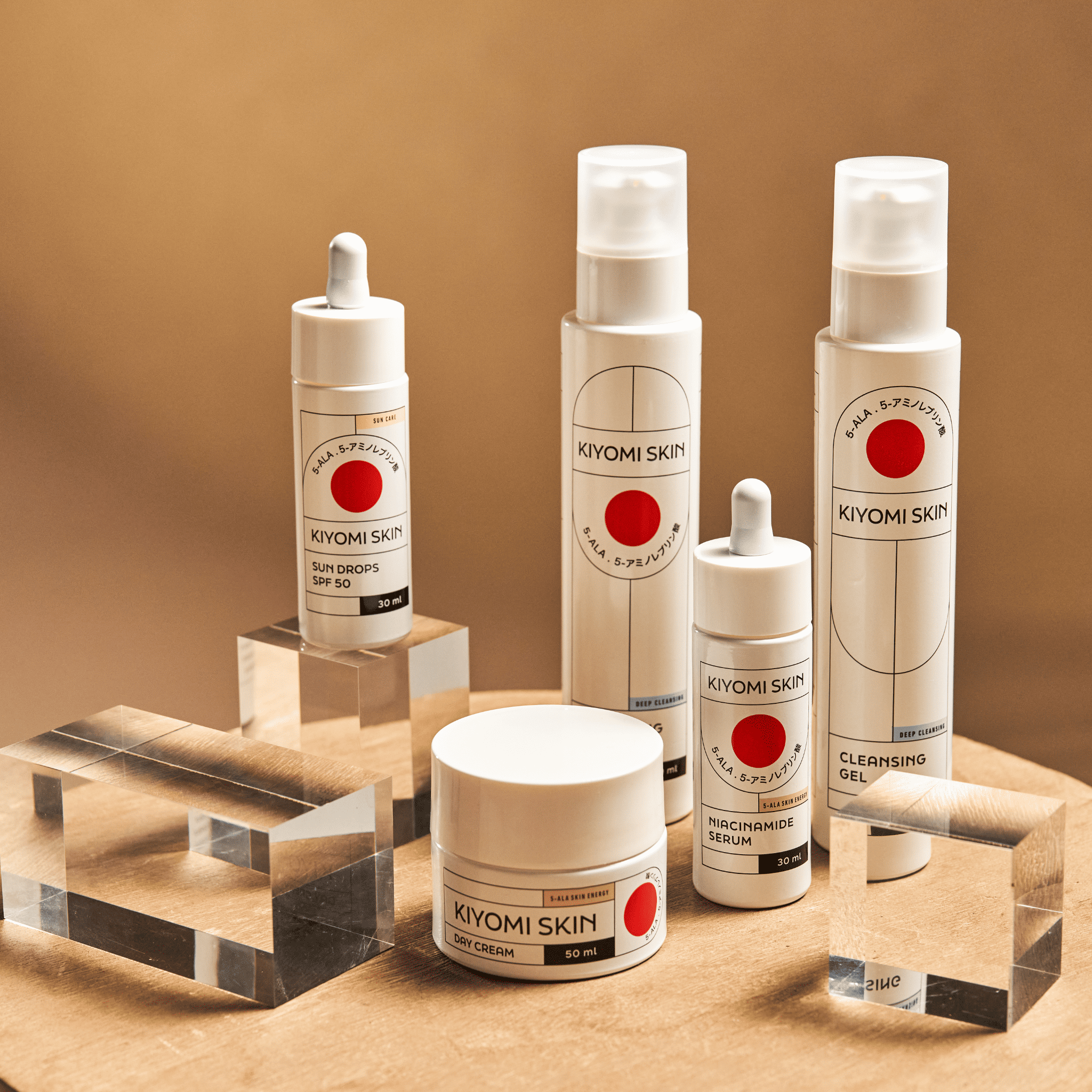Five J-Beauty Glass Skin Must-Haves are displayed on a wooden surface with clear acrylic blocks, highlighting the elegance of Japanese skincare in a sleek 5-step routine.
