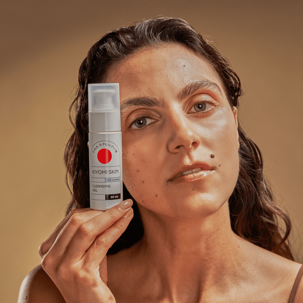 Eine Frau hält eine Flasche „SBI ALApromo Travel Size Cleansing Gel“ – ideal für empfindliche Haut – vor ihrem Gesicht vor einem beigen Hintergrund.