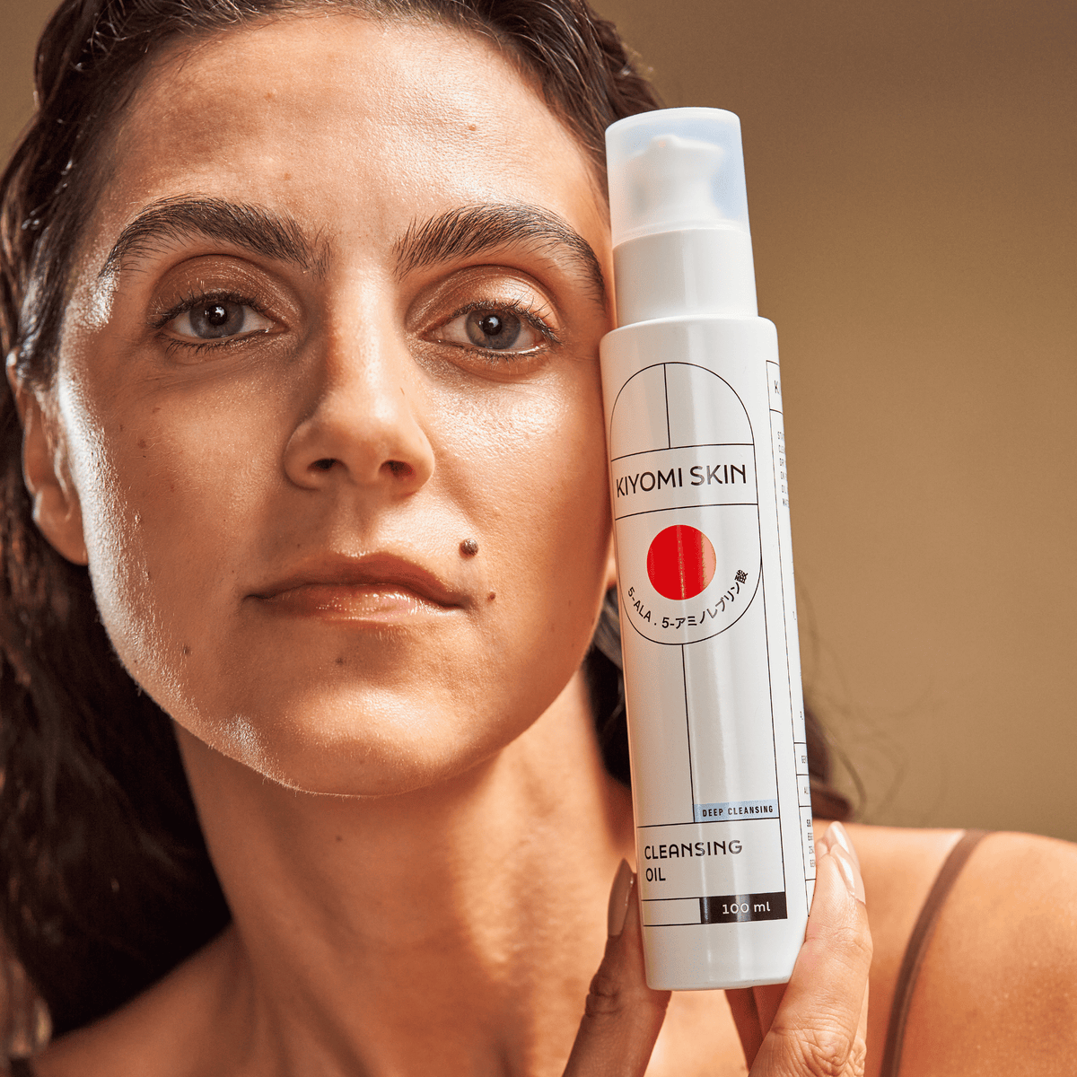 Eine Frau hält eine Flasche „SBI ALApromo Cleansing Oil“ vor ihrem Gesicht vor einem neutralen Hintergrund und blickt direkt in die Kamera – eine ideale Wahl für trockene und empfindliche Haut.