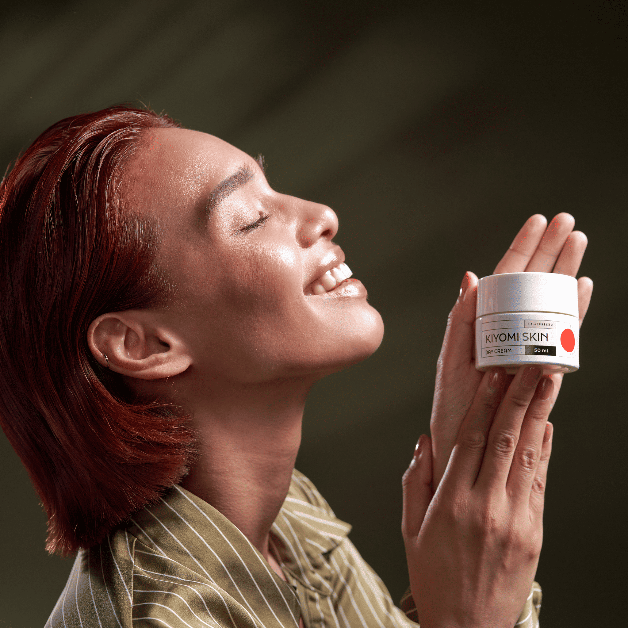 A smiling person with glowing skin holds a Day Cream jar against a soft green background.
