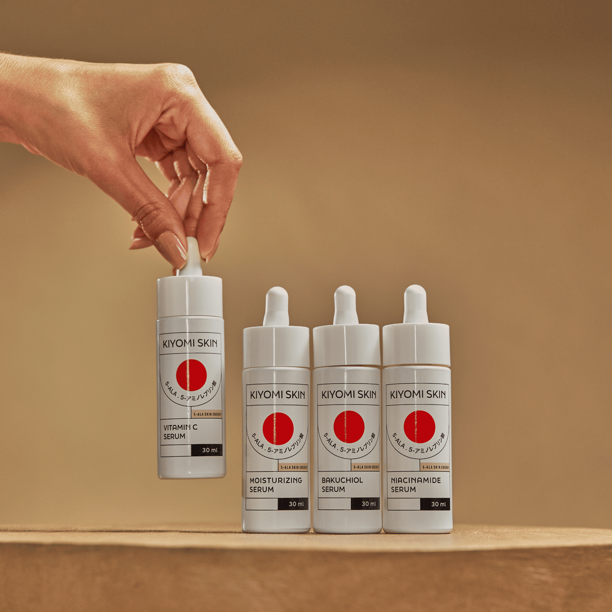A hand picks up a Full Spectrum Serum Kit bottle beside three other skincare bottles, highlighting a complete Serum Kit for your routine.
