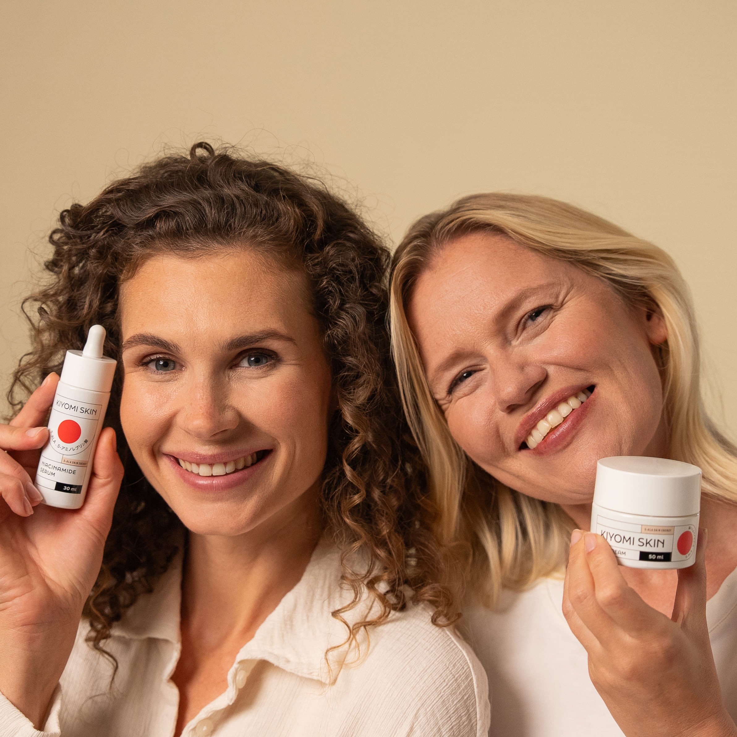 Two women hold small cream containers, showcasing the japanische Hautpflege 5-Schritte-Routine from the J-Beauty Glass Skin Must-Haves Set.
