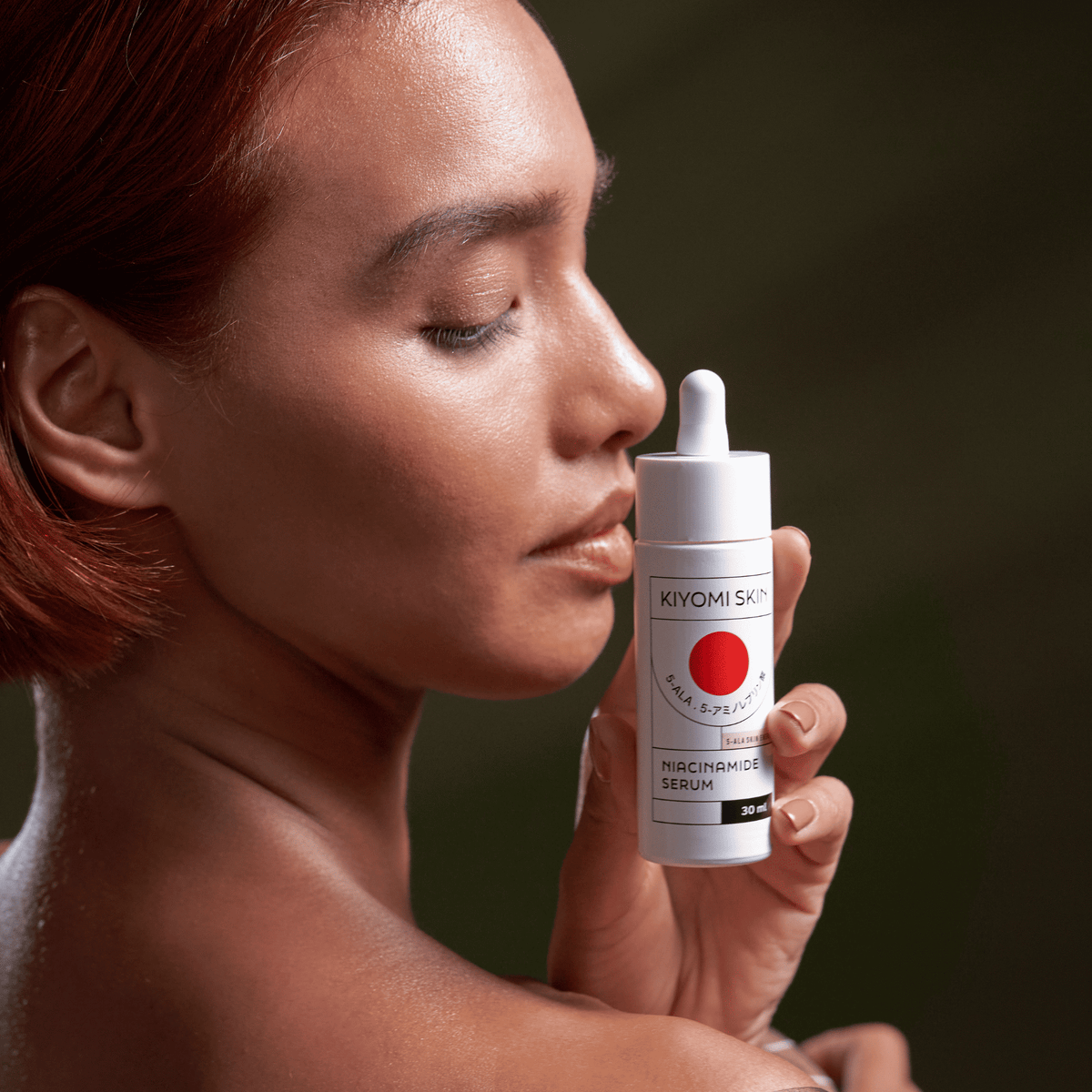 Eine Frau mit strahlender Haut hält eine weiße Flasche des SBI ALApromo Niacinamid-Serums nahe an ihr Gesicht, die Augen geschlossen, und unterstreicht damit die Fähigkeit des Serums, Hautunreinheiten zu reduzieren und vergrößerte Poren sichtbar zu verfeinern.