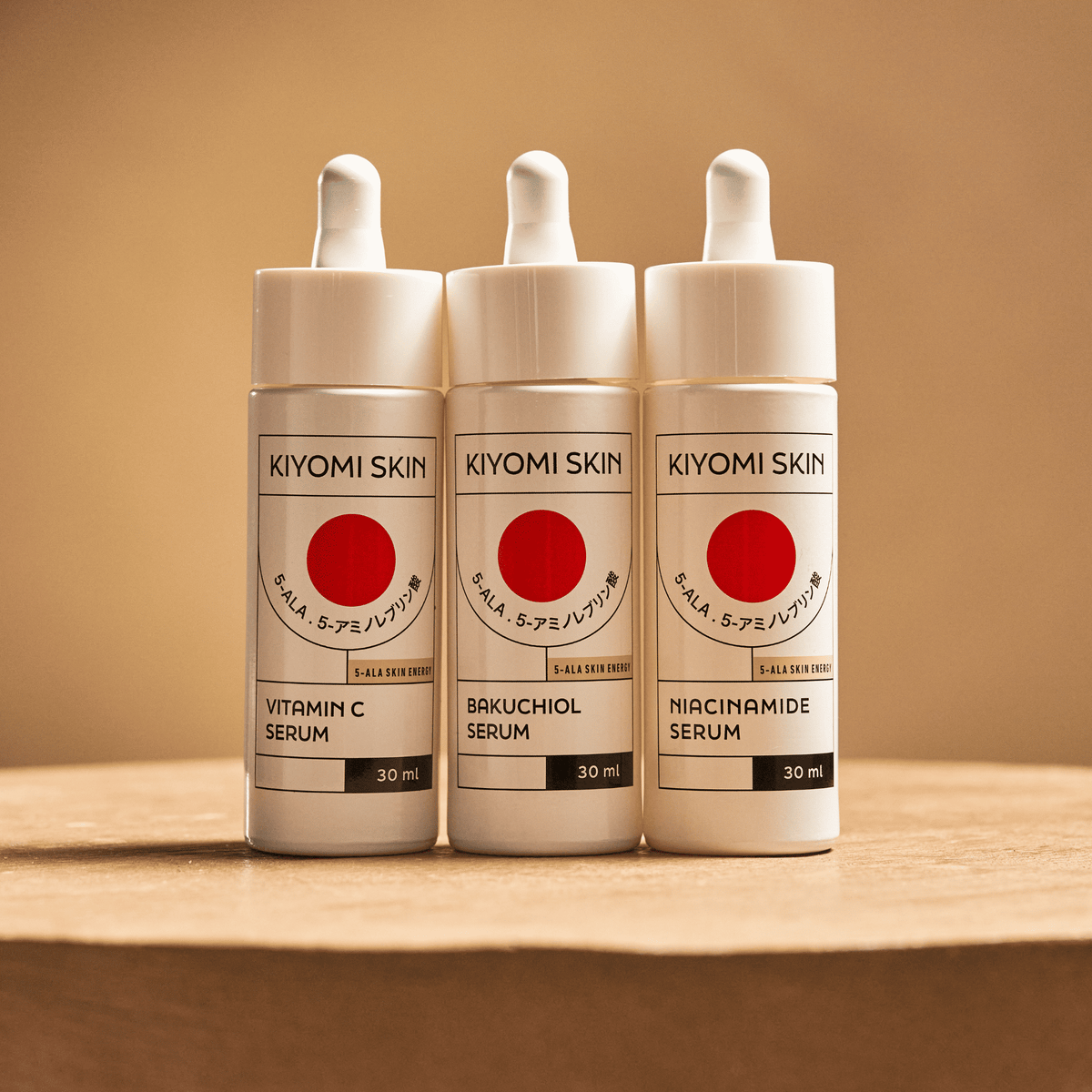 Drei Flaschen der „SBI ALApromo Serum Trilogy Radiance & Renewal“-Serie – Vitamin C, Bakuchiol und Niacinamid – stehen nebeneinander auf einer braunen Unterlage und präsentieren das komplette Set für strahlende und gesunde Haut.