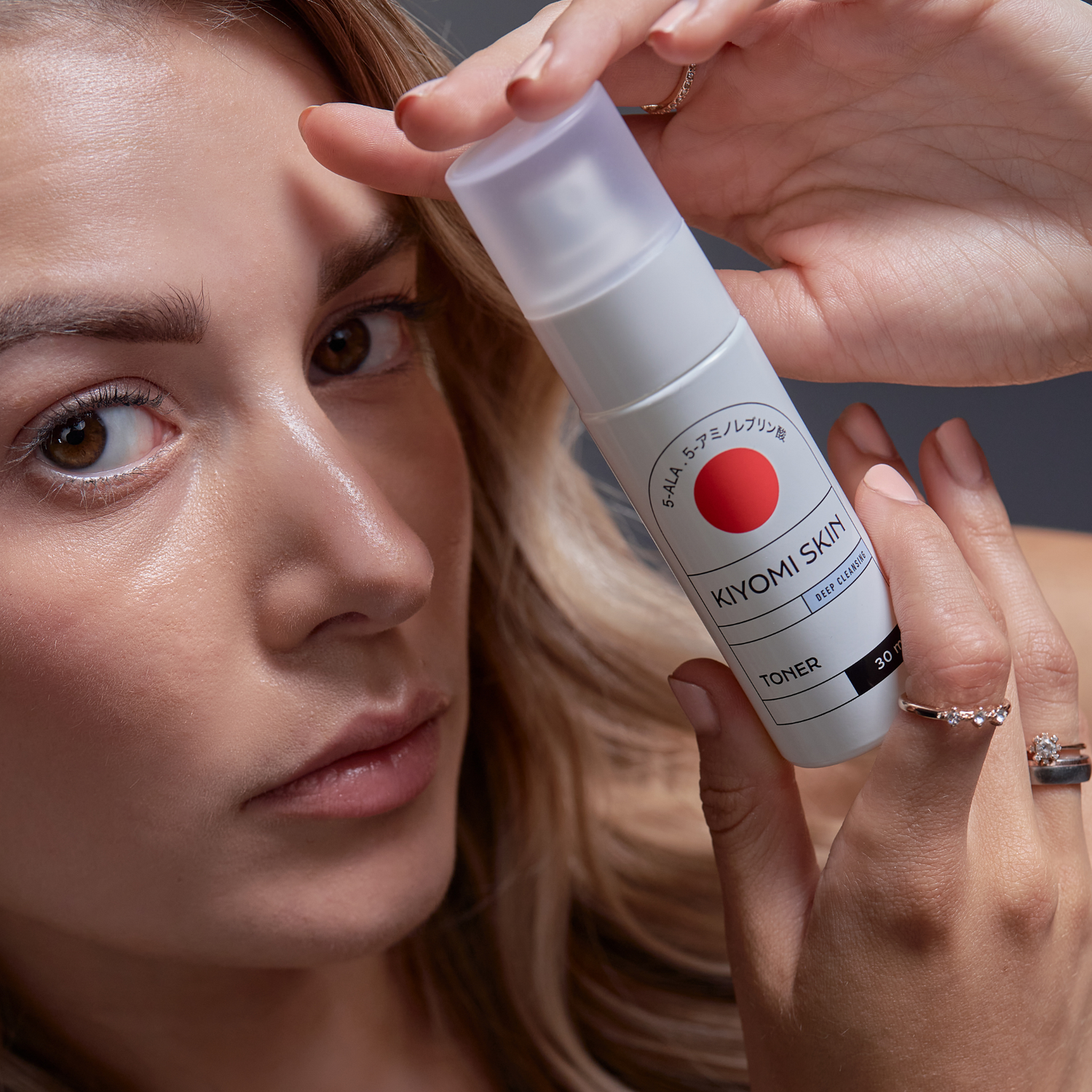 A woman holds a bottle of Travel Size Toner close to her face, showcasing her clear and glowing skin.