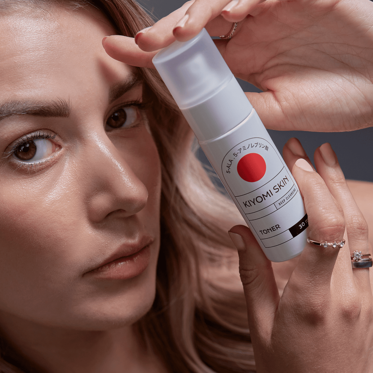 Eine Frau hält eine Flasche „Kiyomi Skin Travel Size Toner“ dicht an ihr Gesicht und zeigt dabei glatte, strahlende Haut – ideal für empfindliche Haut.