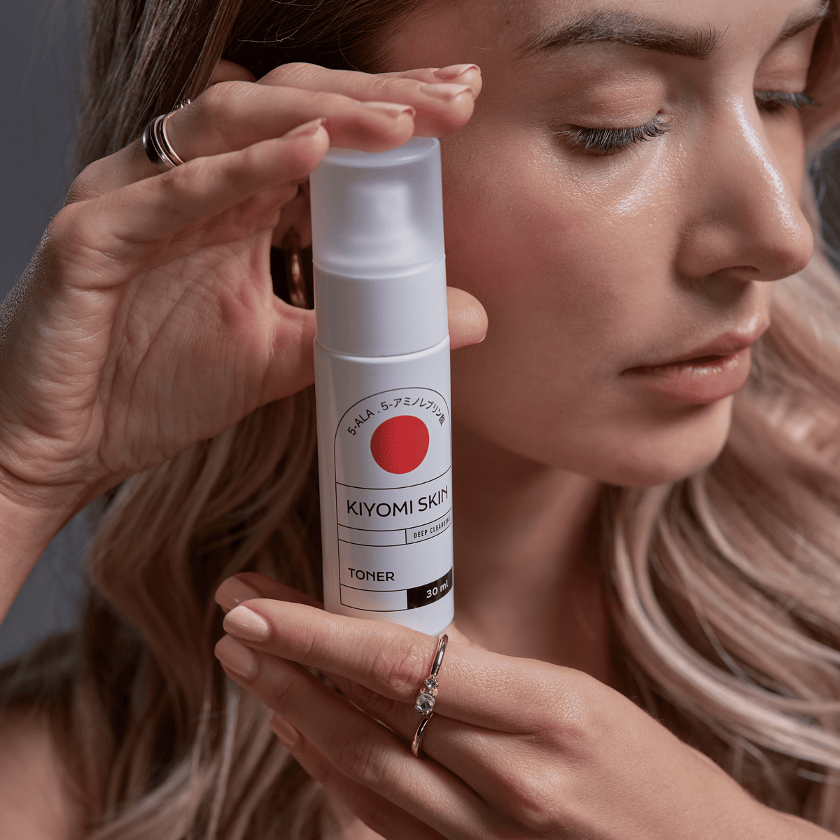 Eine Frau hält eine Flasche „Kiyomi Skin Travel Size Toner“ dicht an ihr Gesicht und zeigt dabei reine Haut und einen sanften Gesichtsausdruck – die perfekte Pflege für empfindliche Haut.